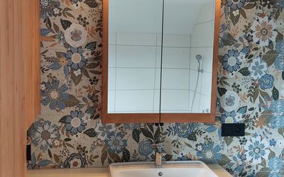 Modernes Badezimmer mit floral gemusterter Rückwand, rechteckigem weißen Waschbecken auf einem Holzunterschrank und beleuchtetem Spiegelschrank darüber.